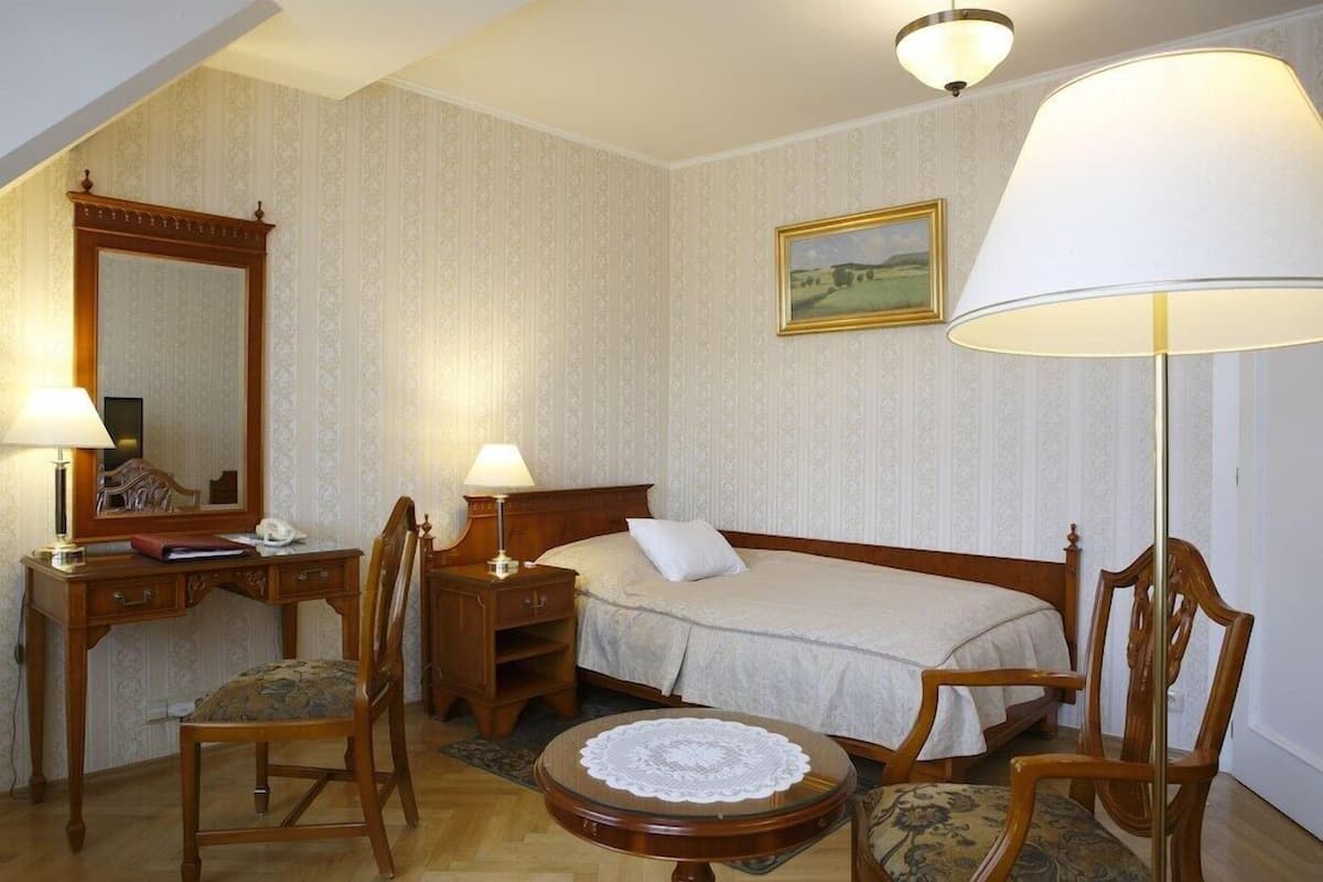 Ein Hotelzimmer mit einem Bett, zwei Stühlen, einem Schreibtisch, einer Lampe, einem Spiegel und einem Bild an der Wand.