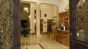 Een hotel lobby met een receptiebalie, een klok aan de muur en een bordje met de tekst 'ISTOL PALACE'.