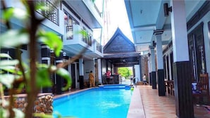 A swimming pool area with a covered seating area and a view of the building's exterior. - VIBOLA Guesthouse (Kampot)