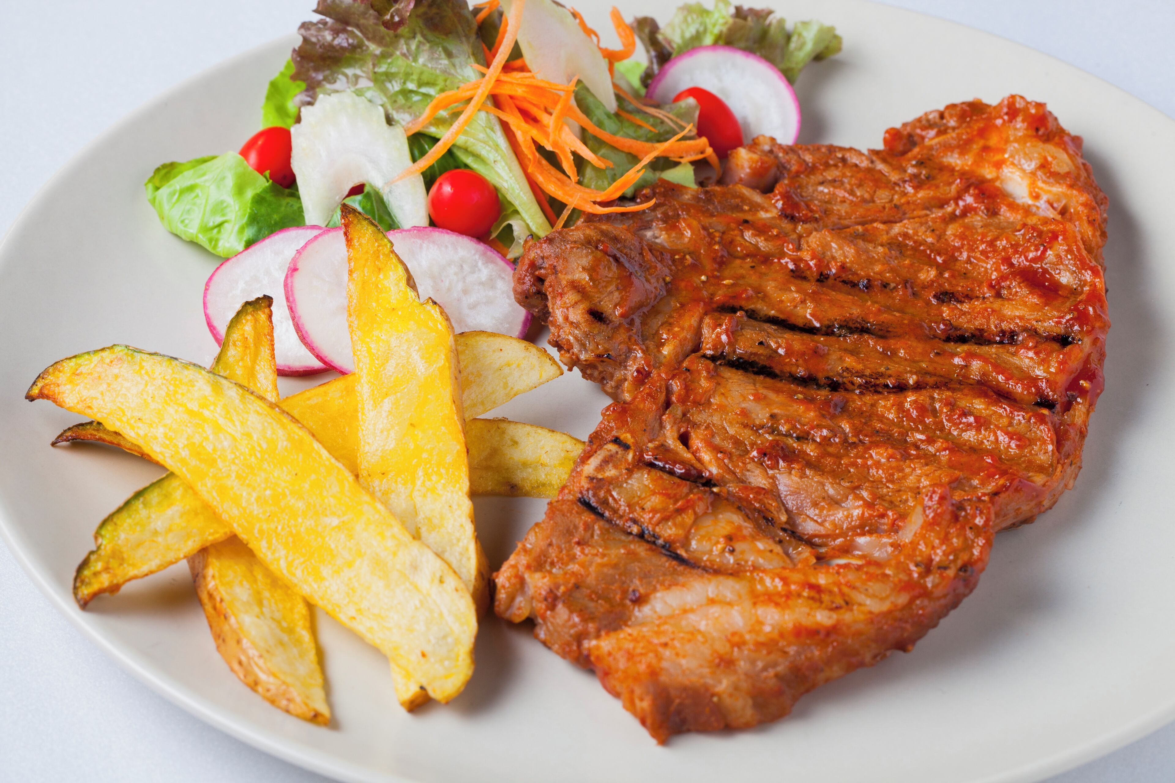 Un plato con carne a la parrilla, papas fritas y una ensalada.