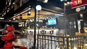 Zona de bar al aire libre con mostrador, asientos y una pantalla grande.