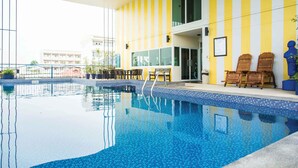 Una piscina con bordes azules de azulejos, sillas de madera y una pared a rayas amarillas y blancas.