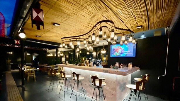 Zona de bar moderna con techo alto, vigas de madera a la vista y una barra central con taburetes.