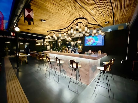 A modern bar area with a high ceiling, exposed wooden beams, and a central bar counter with stools.
