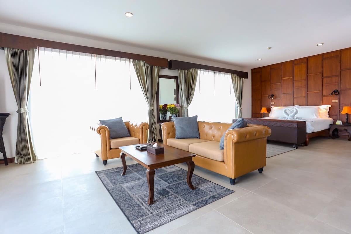 Quarto de hotel com sofá, mesa de centro, cama com edredom branco e mesa de cabeceira com abajur.