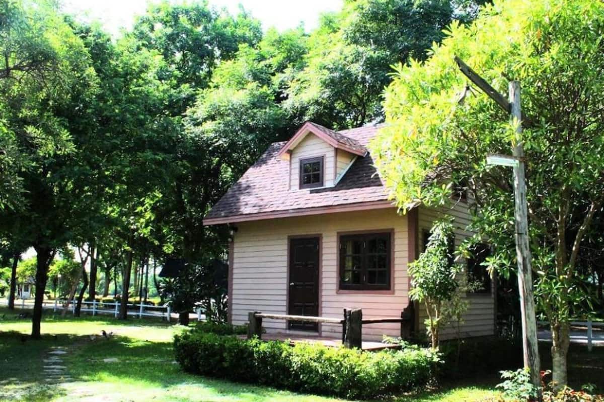 A small, single-story house with a pitched roof, surrounded by lush greenery and trees.