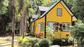 Una casa amarilla de techo a dos aguas, rodeada de follaje y un sendero.