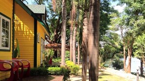 A yellow building with a wooden deck and red chairs, surrounded by palm trees and greenery. - Island Resort River Kwai by October (Kanchanaburi)