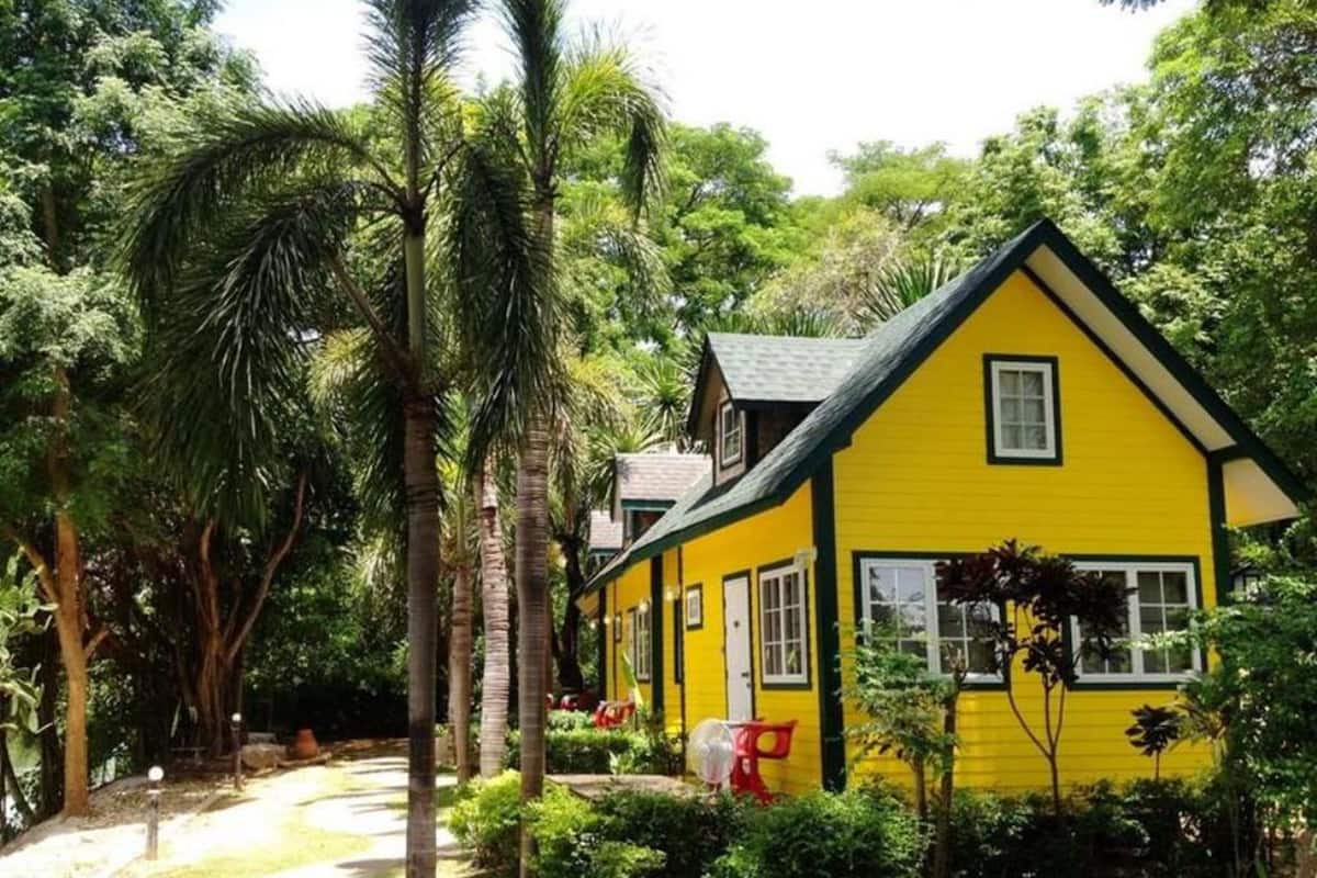 A yellow house with a black roof surrounded by lush greenery and palm trees.