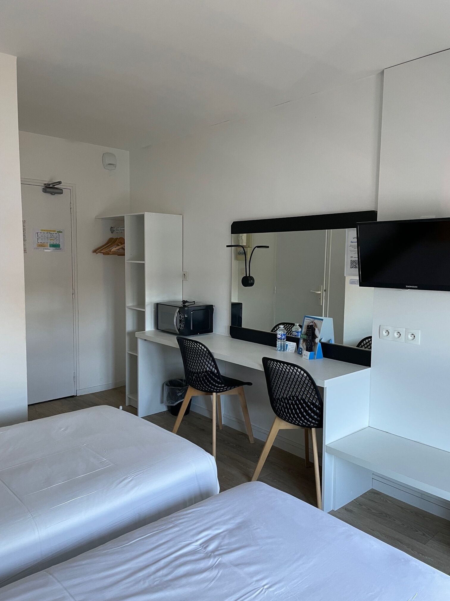 Una habitación de hotel con dos camas, un escritorio con computadora, un televisor y un espejo.