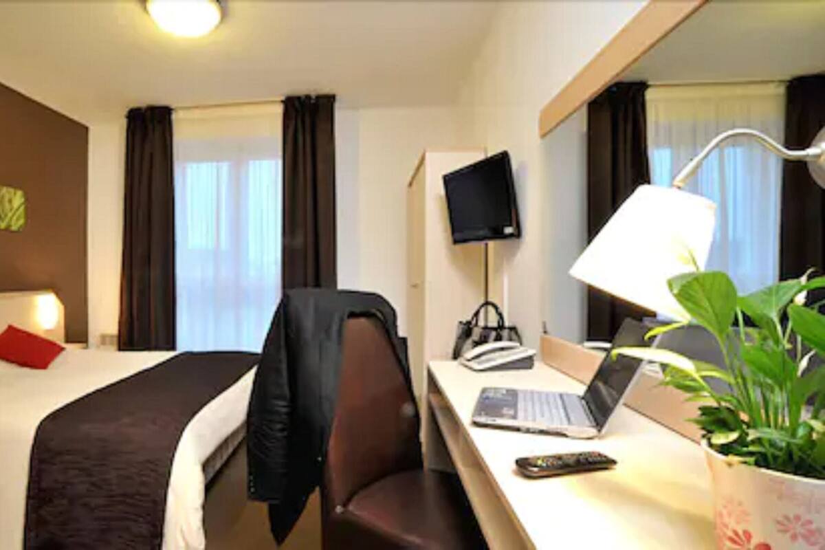 Une chambre d’hôtel avec deux lits, un bureau avec un ordinateur portable, une chaise, une télévision et une plante.