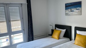 Een hotelkamer met twee bedden, een plafondlamp, een schilderij en een raam met zonwering.