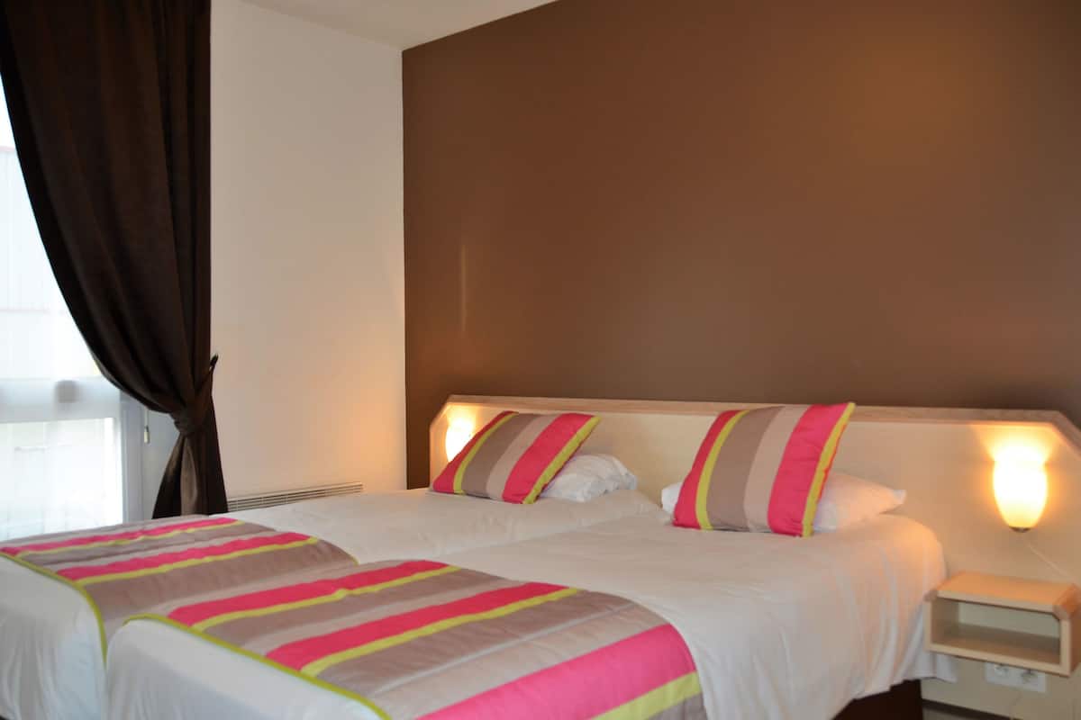 Une chambre d’hôtel avec deux lits, une table de chevet et une fenêtre avec des rideaux.