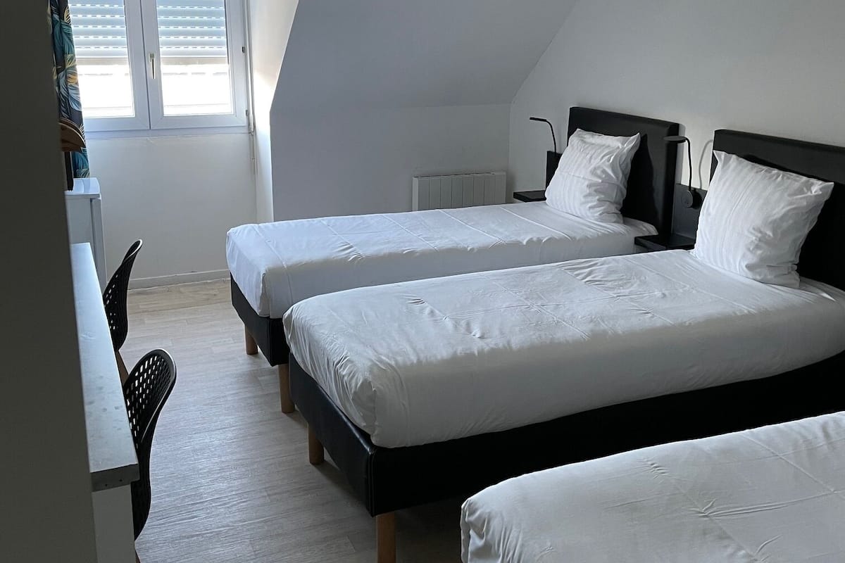 Une chambre avec deux lits, un bureau et une fenêtre avec des stores.