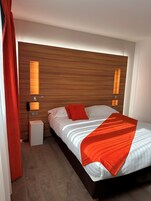 A hotel room with a wooden headboard, a bed with white and orange bedding, two bedside lamps, and a telephone on the nightstand.