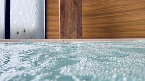 Een wellnessruimte met een houten wand, een decoratief houten sculptuur en een bruisende jacuzzi.