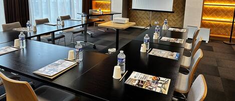 A conference room with tables, chairs, water bottles, and a projector screen.