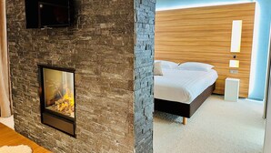 Een kamer met een stenen muur, een openhaard, een bed met wit beddengoed en een houten hoofdbord.