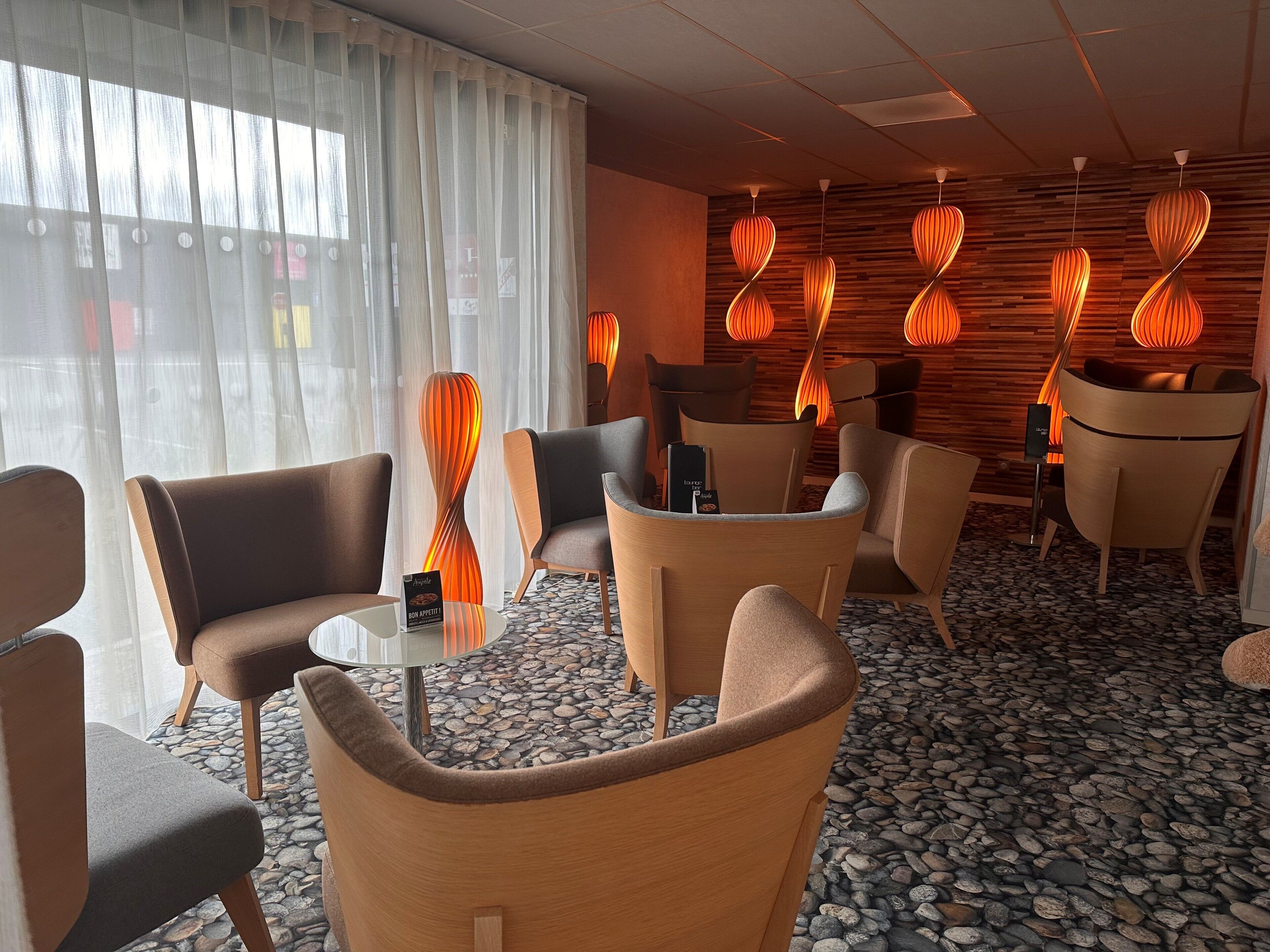 Un hall d’hôtel moderne, doté de meubles contemporains, d’un sol carrelé en pierre et d’un éclairage chaleureux.