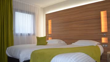 A hotel room with two beds, a wooden headboard, and a window with sheer curtains.