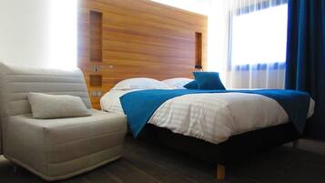 Een hotelkamer met een bed, een stoel, een houten hoofdbord en een raam met gordijnen.