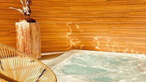 Een wellnessruimte met een jacuzzi, houten wanden en een rieten stoel.