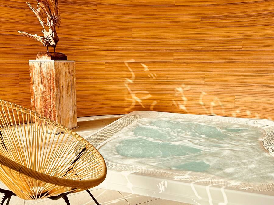 Un espace bien-être comprenant un jacuzzi, des murs en bois et un fauteuil en osier.