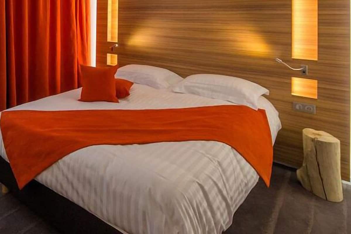 Ein Hotelzimmer mit Bett, orangenen Vorhängen und einem Holzkopfschild mit Wandleuchten.