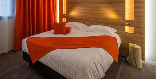 A hotel room with a bed, orange curtains, and wooden headboard with wall-mounted lights.