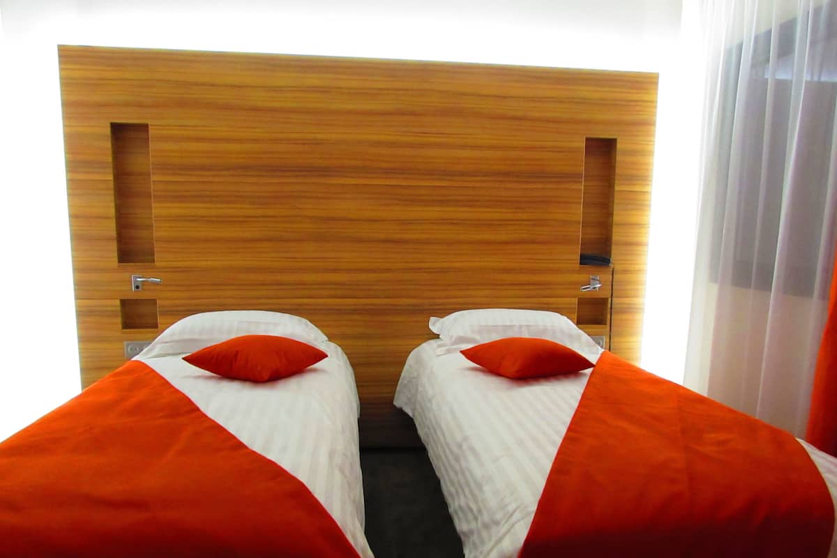 Ein Doppelzimmer mit zwei Betten, jeweils mit weißer Bettwäsche und orangefarbenen Kissen.