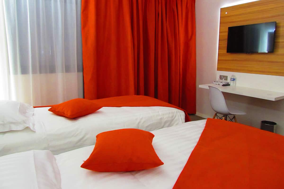 Ein Hotelzimmer mit zwei Betten, einem Schreibtisch, einem Sessel und einem Fernseher an der Wand.