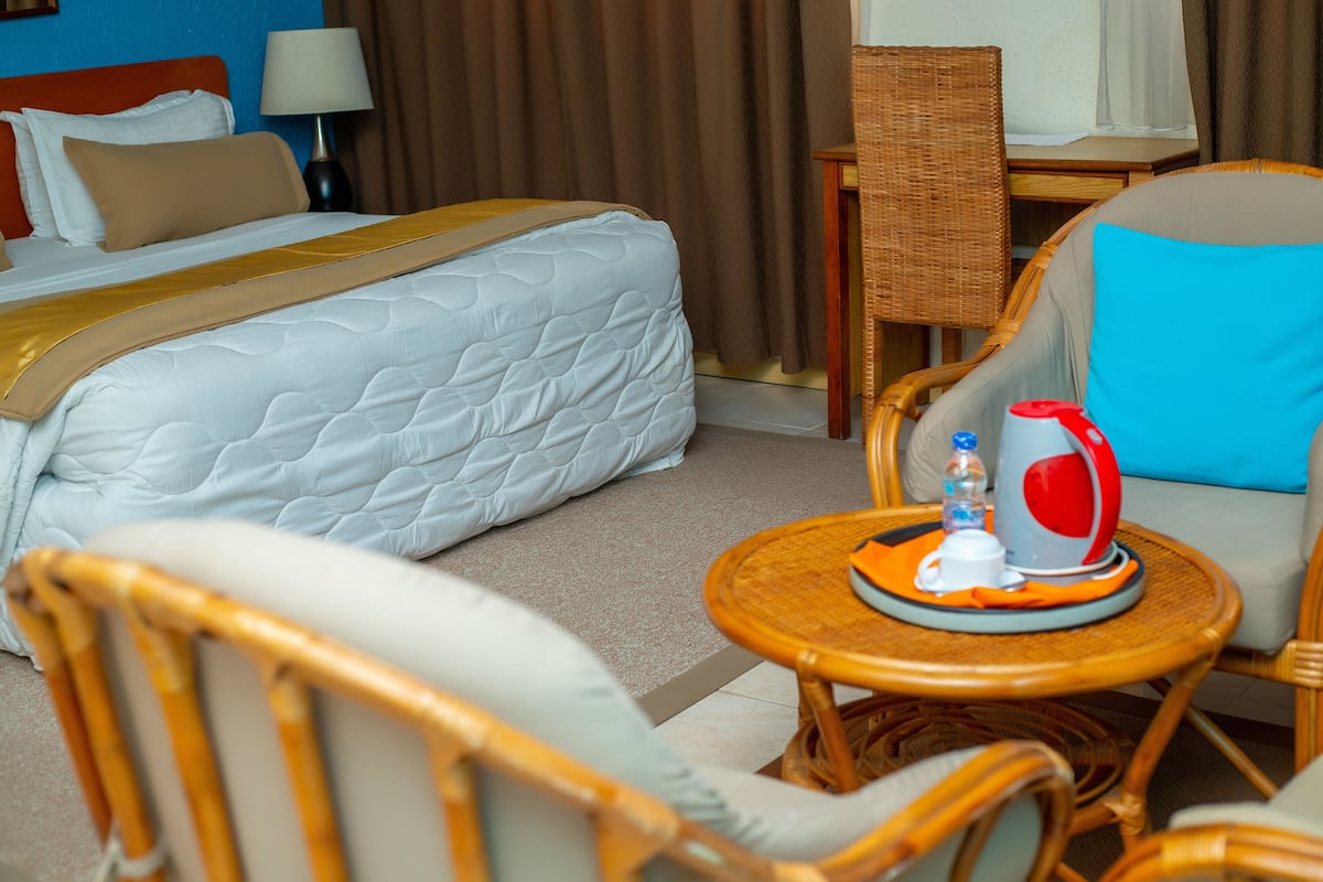 A hotel room with a bed, a chair, a table with a kettle, and a bottle of water.