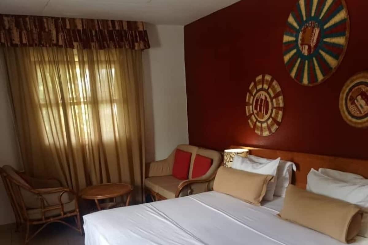 A hotel room with a large bed, a sofa, a small table, and curtains.