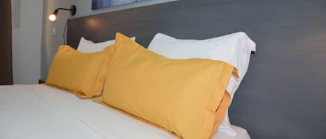 A neatly made bed with white and yellow pillows, a gray headboard, and a wall-mounted lamp.