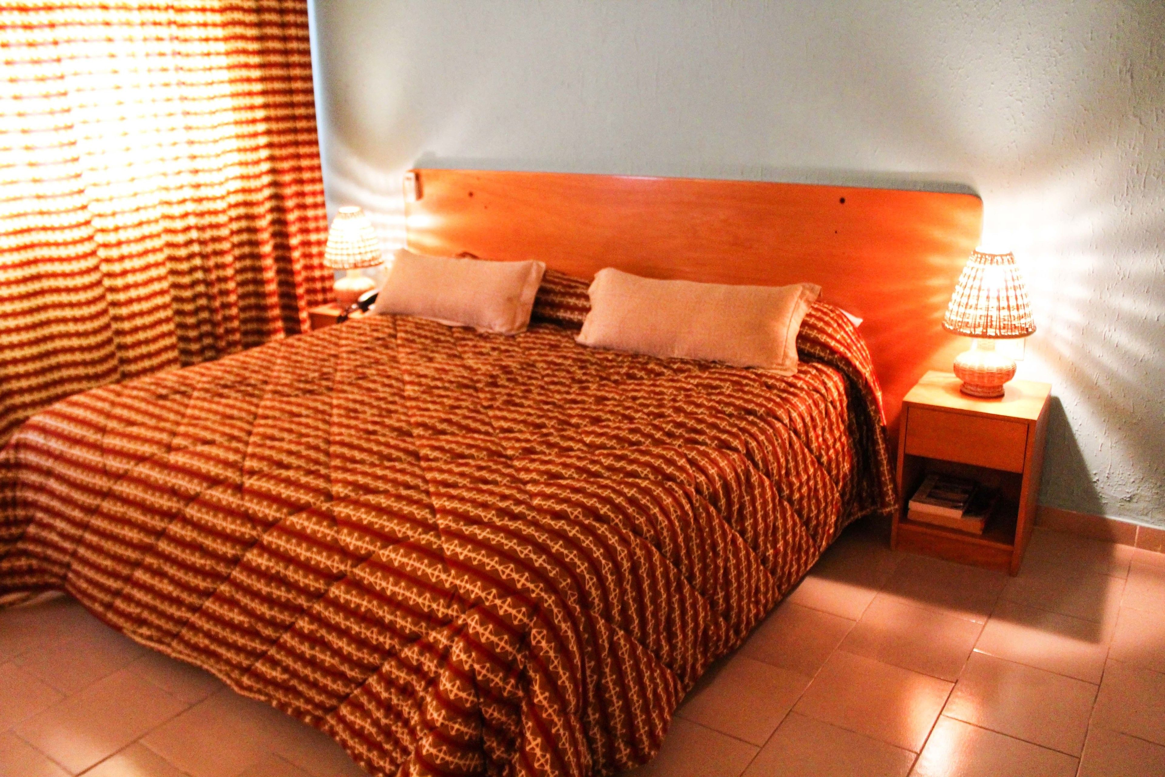 A neatly made bed with a striped bedspread, two pillows, and a nightstand with a lamp.