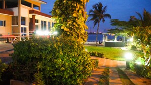 A well-lit hotel with a modern design, featuring a large central column, a pool area, and a view of the sea.