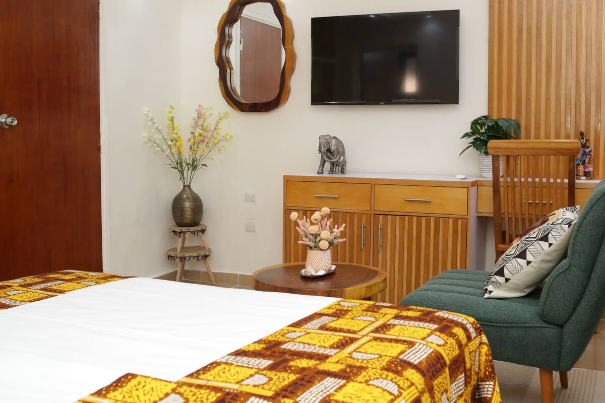 A hotel room with a bed, a green sofa, a wooden desk, a television, and a decorative elephant statue.