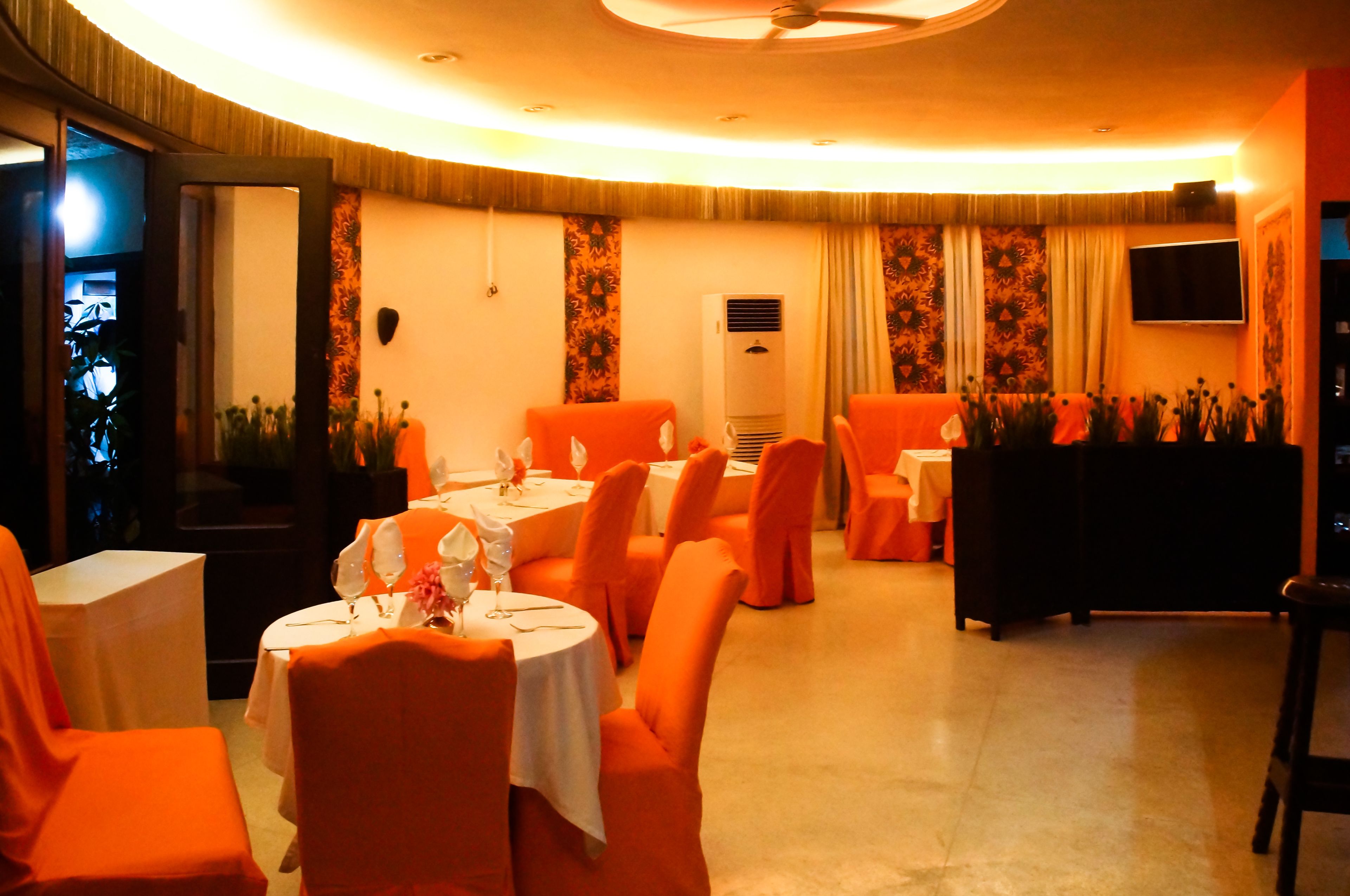 Ein Restaurant mit runden Tischen, orangefarbenen Stühlen und einem Deckenventilator.