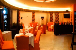 Un restaurante con mesas redondas, sillas naranjas y un ventilador de techo.