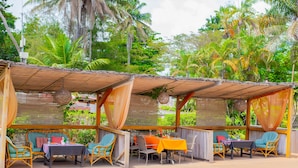 A covered outdoor seating area with wicker furniture and a pool in the background.