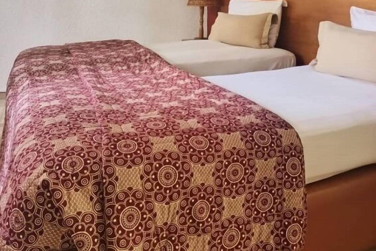 A hotel room with two beds, a large bed with a patterned bedspread and two smaller beds with plain linens. There are decorative plates on the wall and a framed picture above the beds.