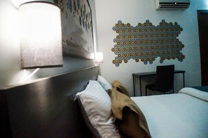 Habitación de hotel con una cama, cabecero, una obra de arte en la pared, decoración mural estampada, escritorio y una silla.