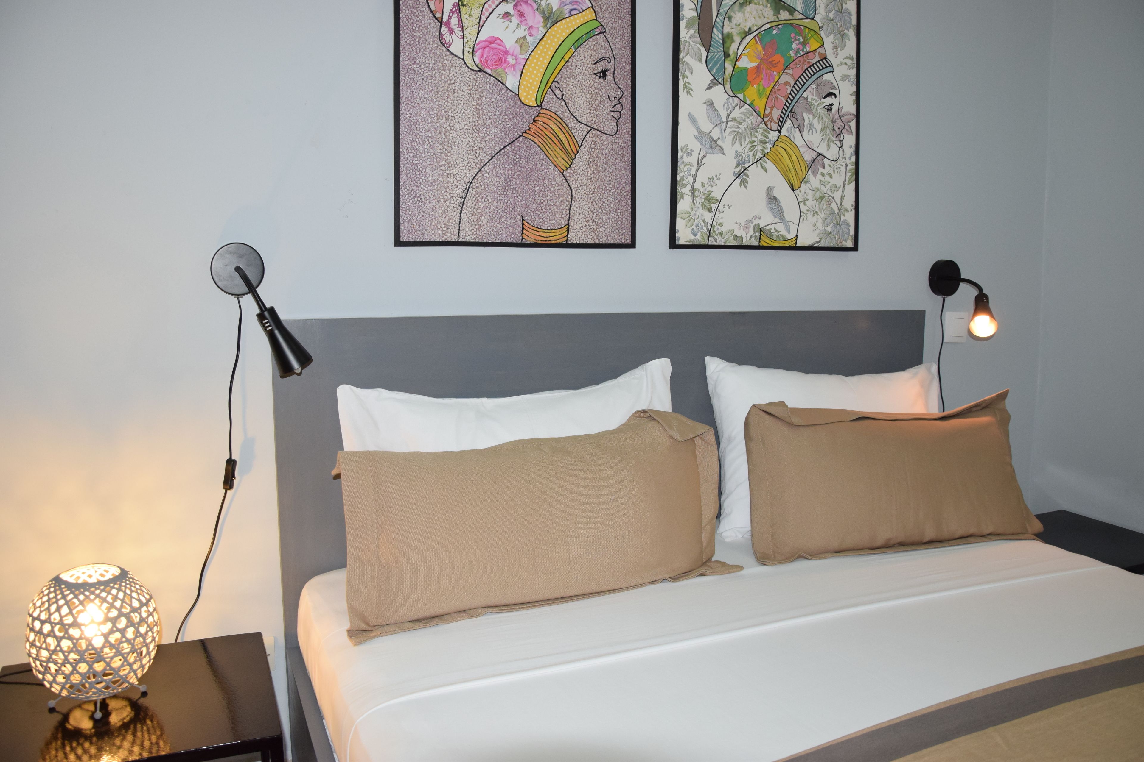 A neatly made bed with two pillows, a headboard, and two wall-mounted lamps.