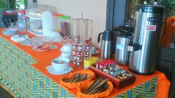 A breakfast buffet setup with various food items, utensils, and beverage dispensers.