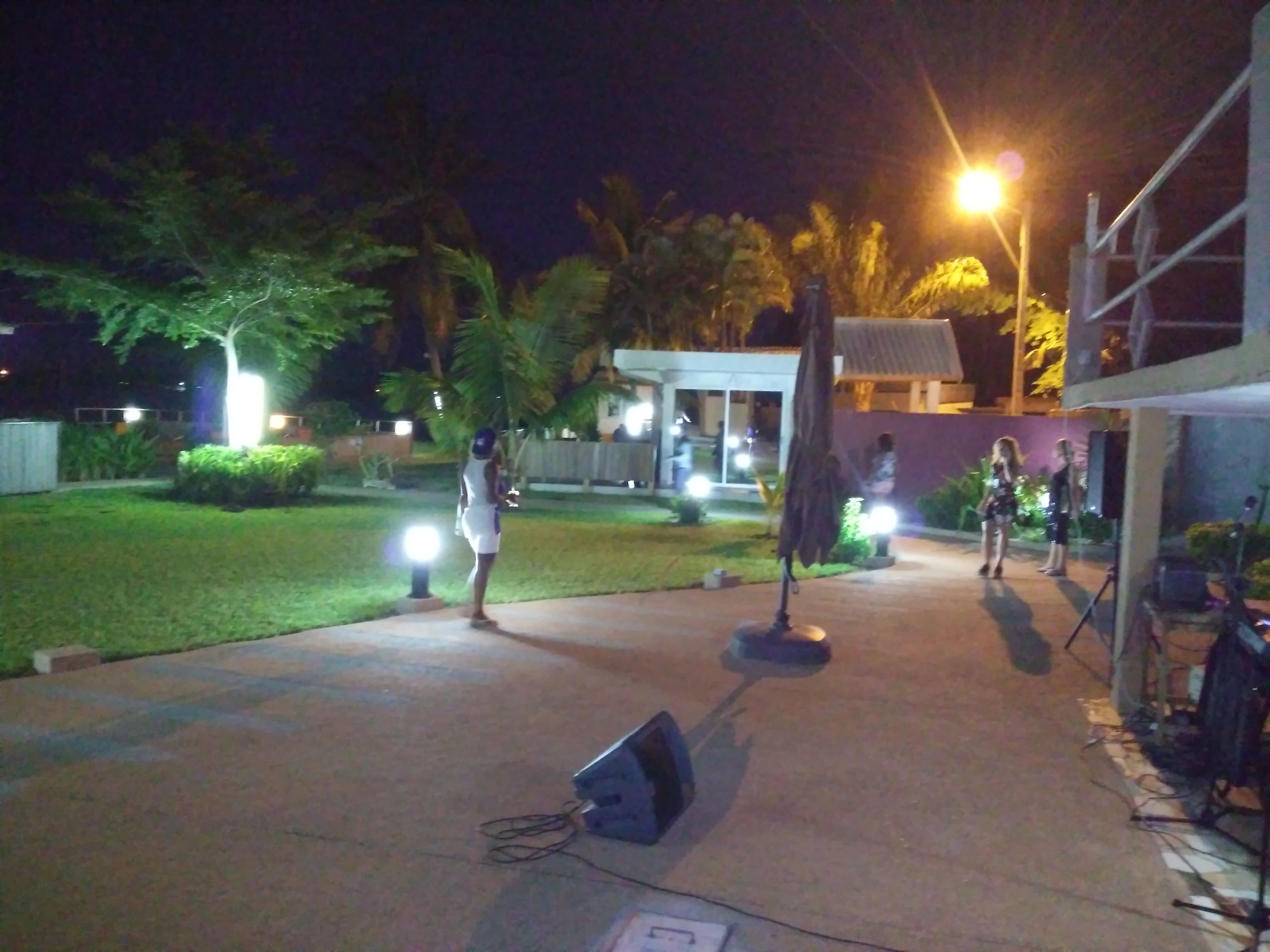 An outdoor area with a paved walkway, a small stage with speakers, and a building in the background.