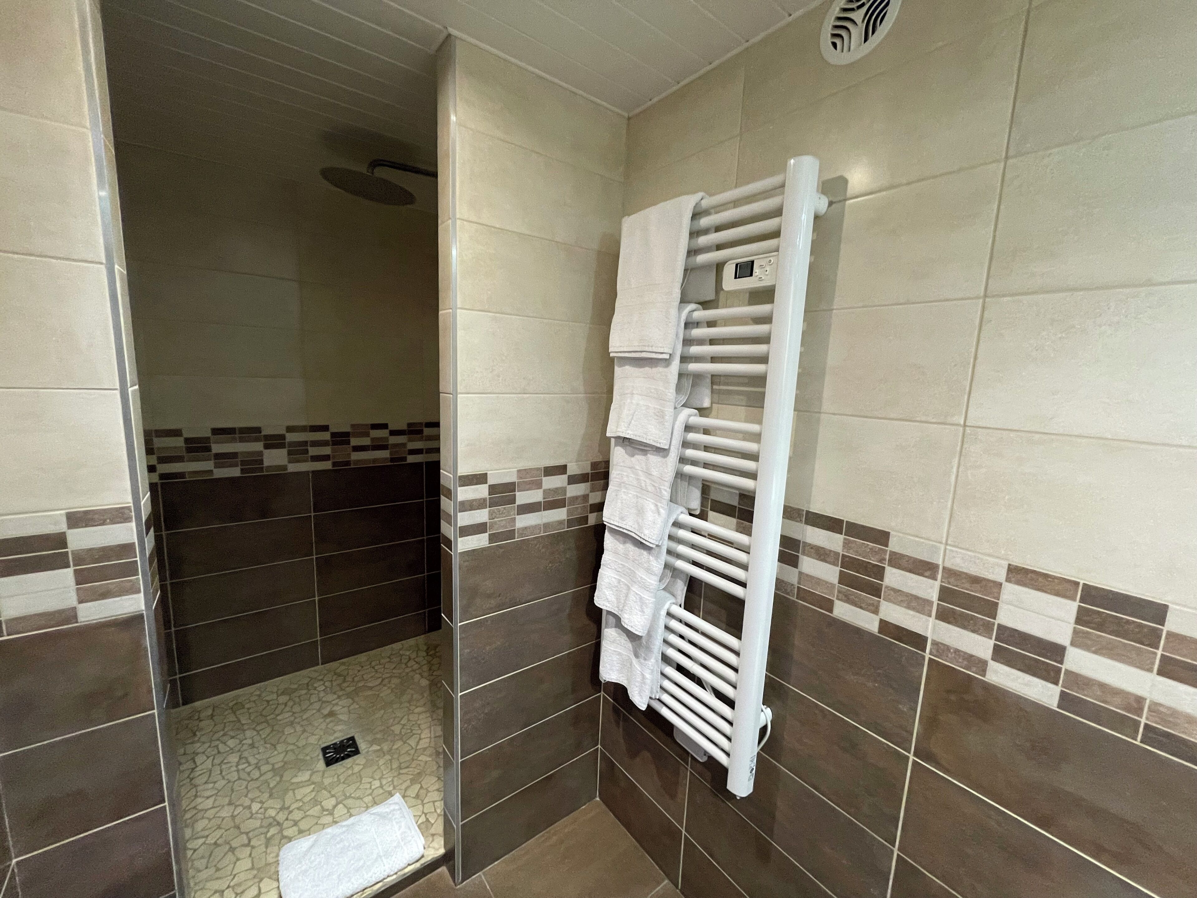 A bathroom with a shower, a white towel rack, and a tiled floor.
