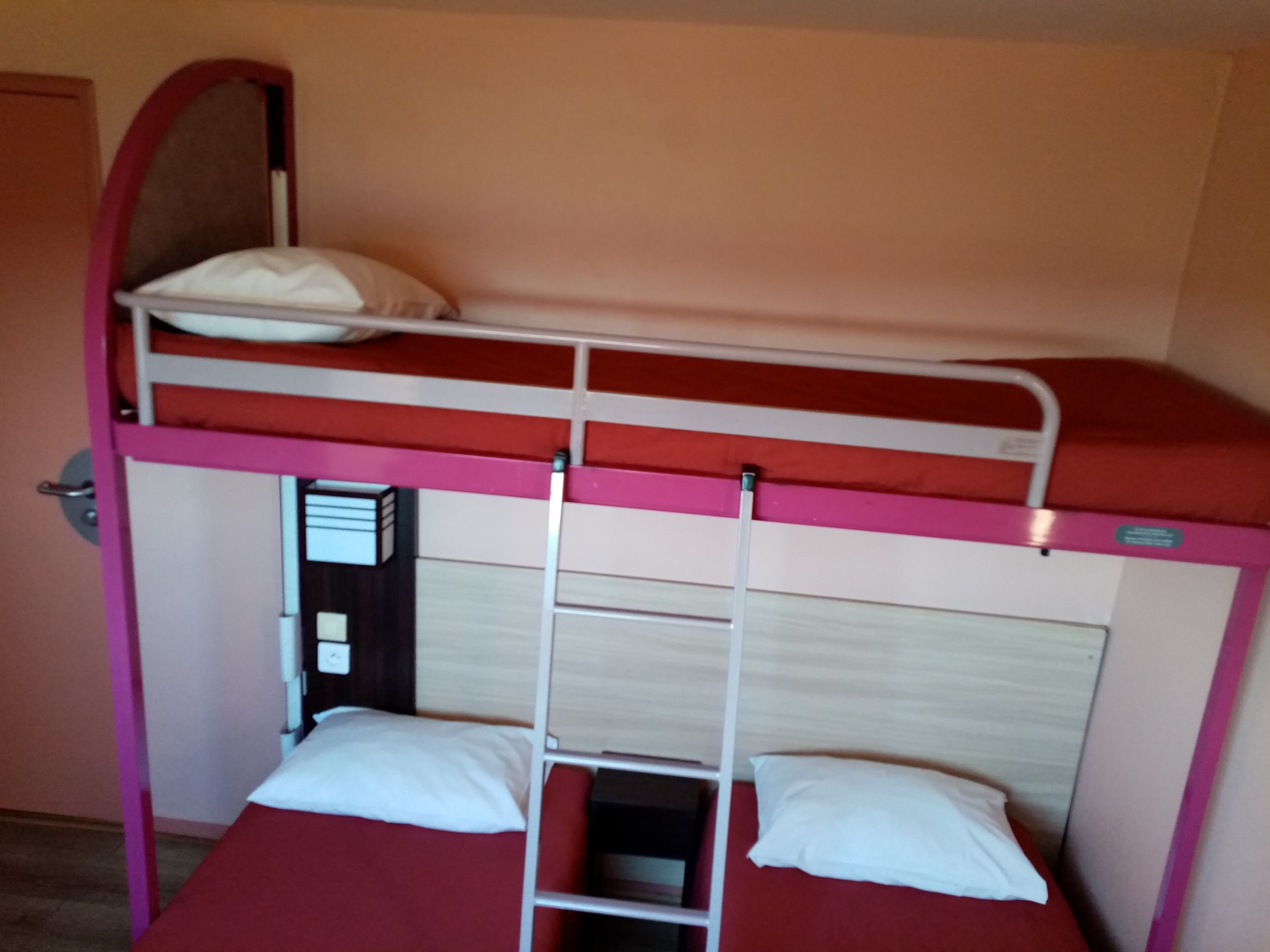 Una cama litera con escalera, una cama individual debajo y una puerta a la izquierda.