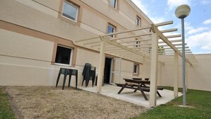 A covered outdoor area with a picnic table and chairs, a lamp post, and a building with multiple windows. - Brit Hotel Saint-Quentin (Fayet)