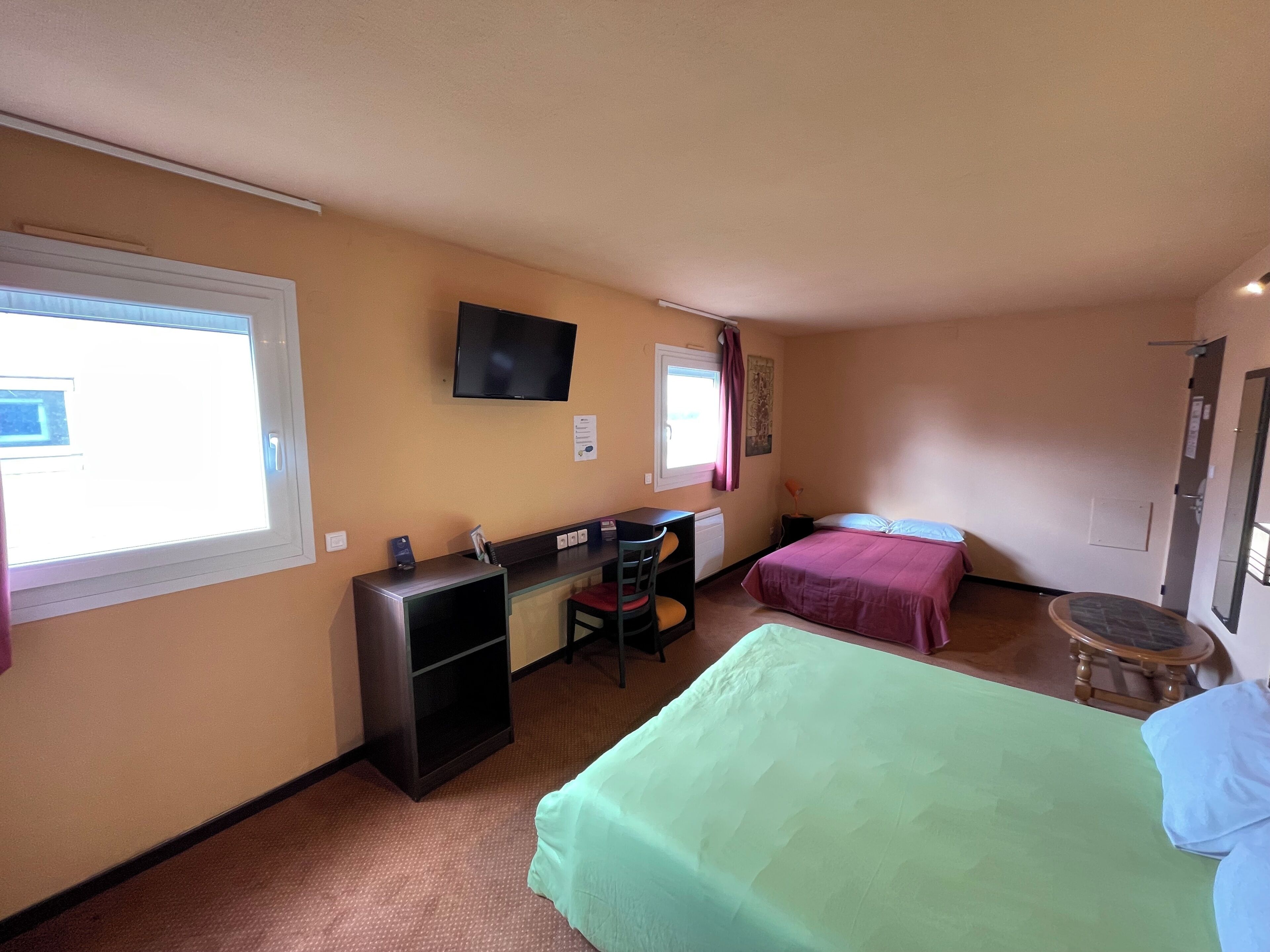 Habitación de hotel con dos camas, un escritorio con silla, televisor montado en la pared y ventana con cortinas.