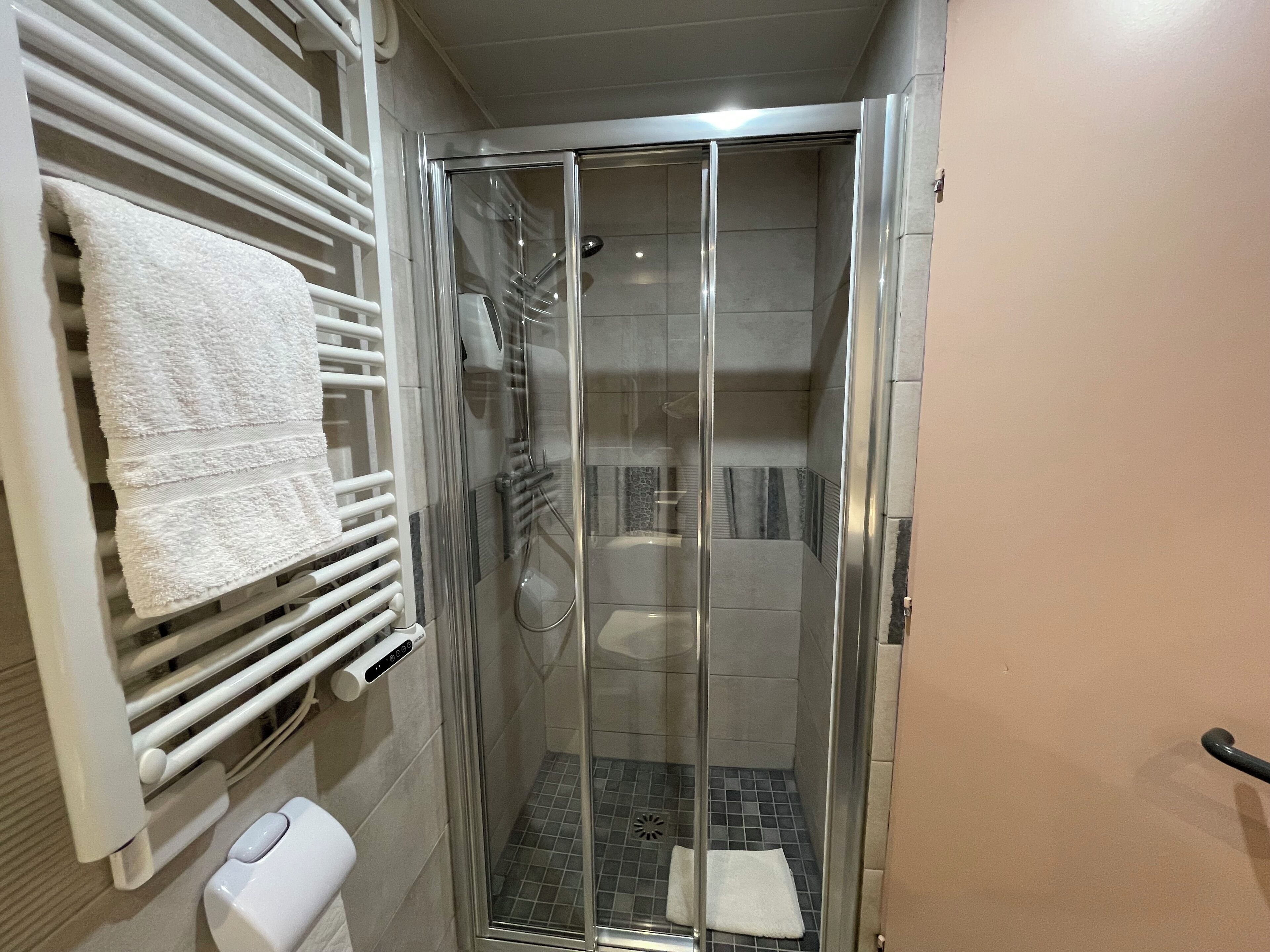 A bathroom with a glass-enclosed shower, a white towel rack, and a toilet.